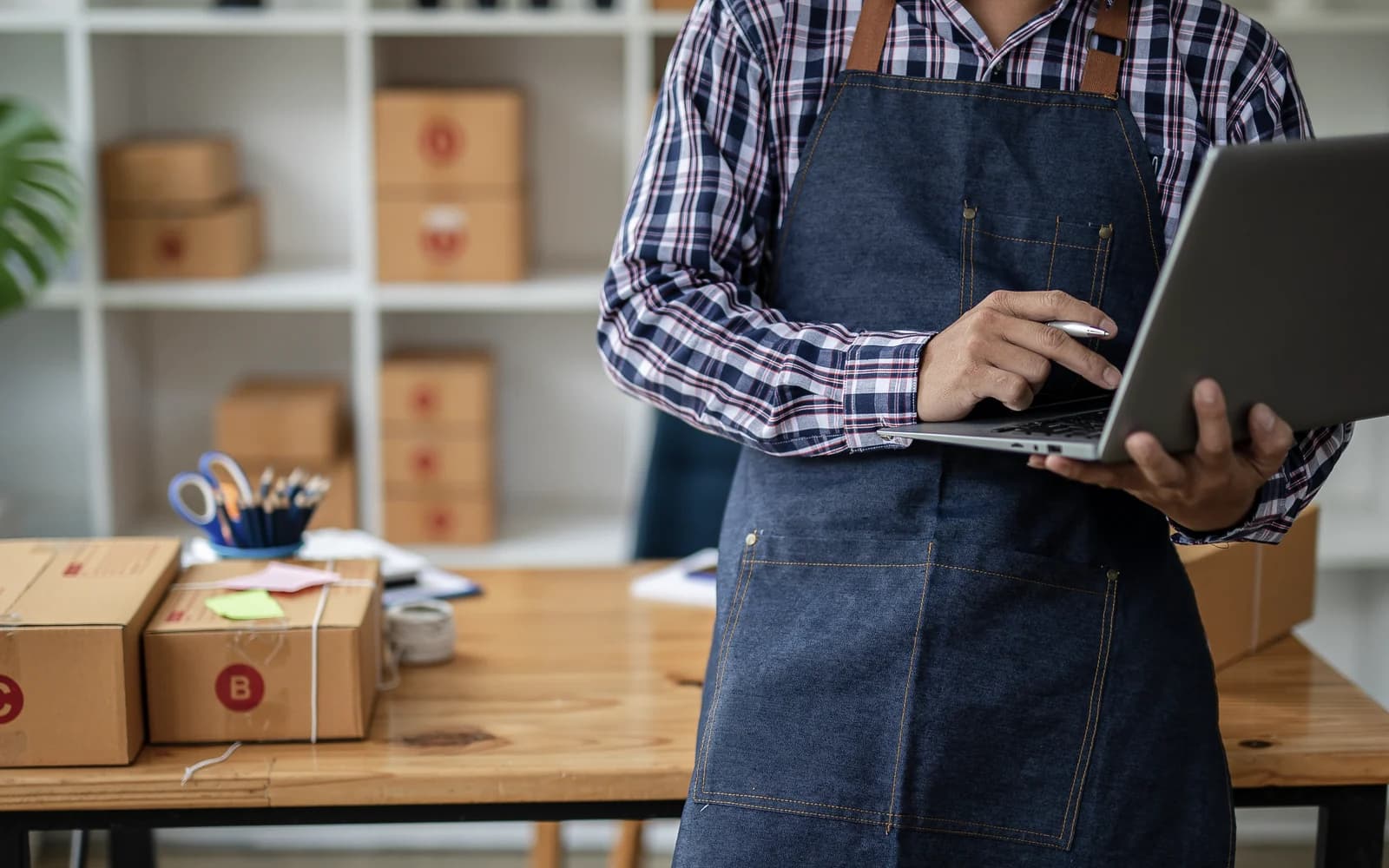 Small-business operator checking orders on a laptop beside packed boxes